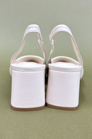 Pair of white pointed-toe slingback shoes on a green background