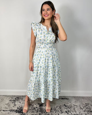 Model wearing a white floral tiered midi dress with flutter sleeves and a smocked waist, styled with nude block-heel sandals.