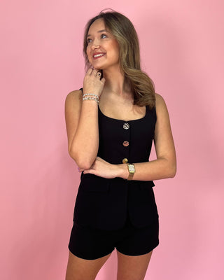 Woman wearing a black outfit with buttons against a pink background
