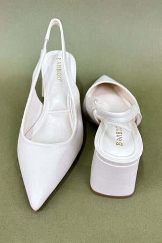 Pair of white pointed-toe slingback shoes on a green background