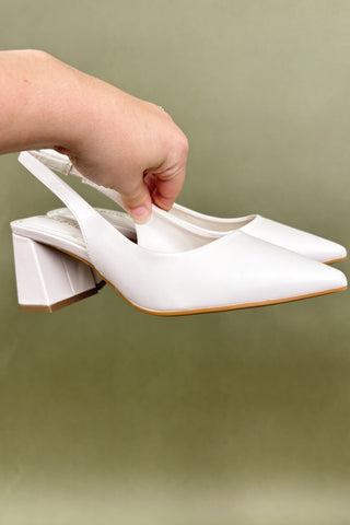 White high-heeled shoes being held against a plain background