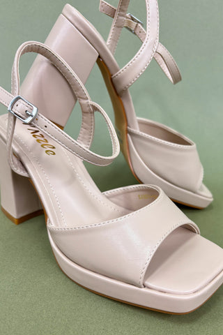 Pair of beige high-heeled sandals on a green background