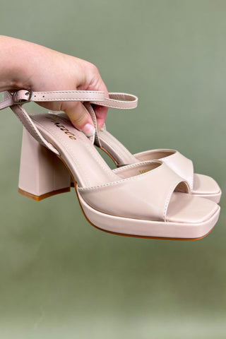 Beige high-heeled sandal held by a hand against a green background