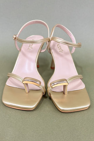 Pair of pink high-heeled sandals with gold straps on a gray background