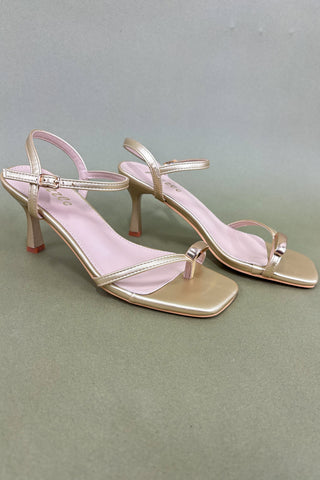 Gold high-heeled sandals on a gray background