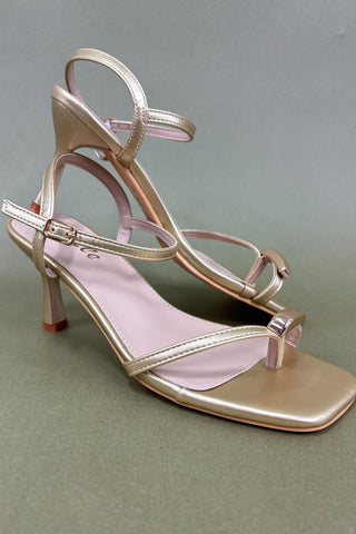 Gold high-heeled sandal on a gray background