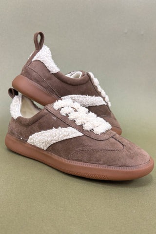 Brown sneakers with white lace-up details on a green background