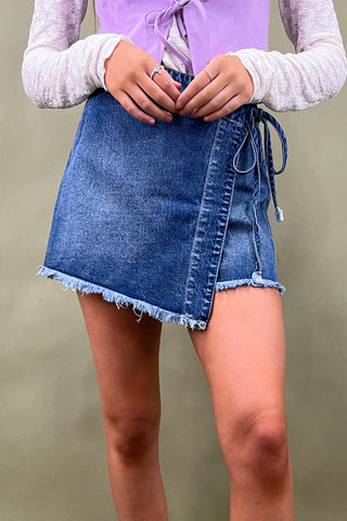 Person wearing a blue denim skirt with a plain background
