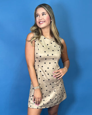 Taupe sleeveless mini dress with black polka dots, round neckline, and flattering A-line silhouette.