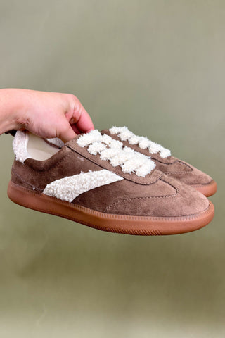 Brown shoes with white laces held by a hand against a green background