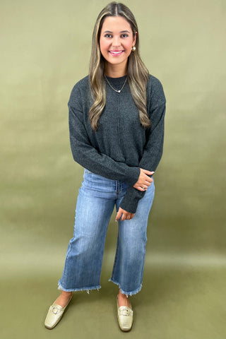 Woman wearing a dark gray sweater and blue jeans against a green background