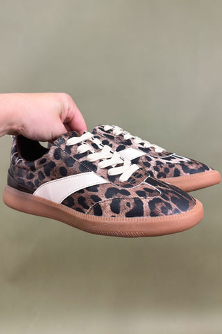 Leopard print sneakers with white laces held by a hand against a plain background