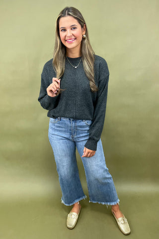 Woman wearing a dark gray sweater and blue jeans against a green background
