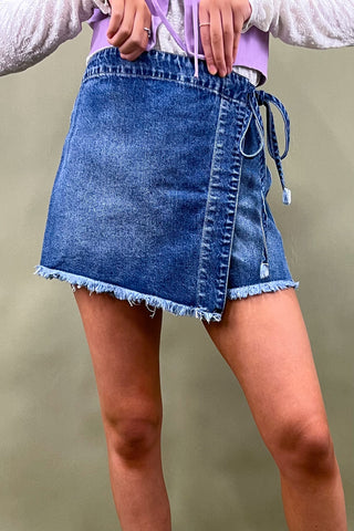 Person wearing a blue denim skirt with a plain background