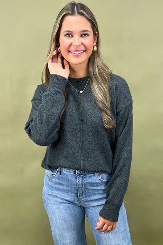 Woman wearing a dark gray sweater and blue jeans against a beige background