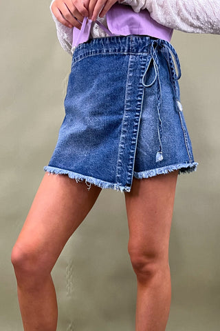 Person wearing a blue denim skirt with a plain background