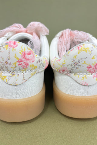 Pair of white sneakers with floral patterns on a green background