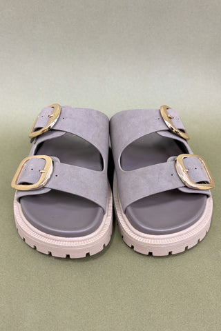 Pair of gray sandals with gold buckles on a light green background