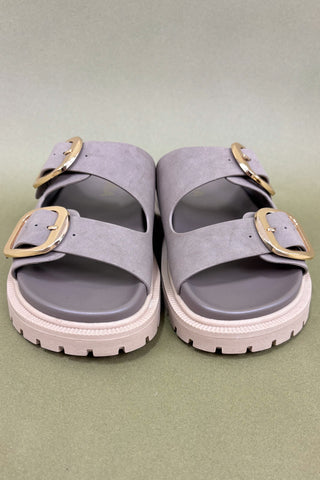 Pair of lavender sandals with gold buckles on a light green background
