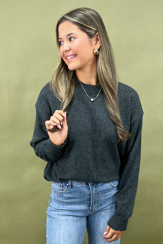 Woman wearing a dark gray sweater and light blue jeans against a green background