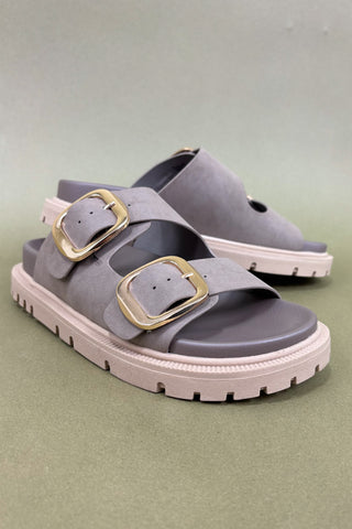 Gray sandals with gold buckles on a green background