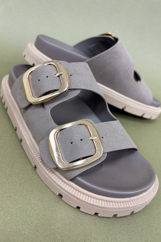 Gray sandals with gold buckles on a green background