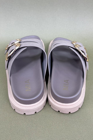 Pair of purple sandals with gold buckles on a green background