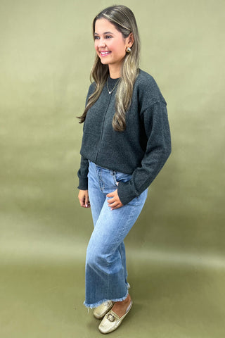 Woman wearing a dark gray sweater and blue jeans on a beige background