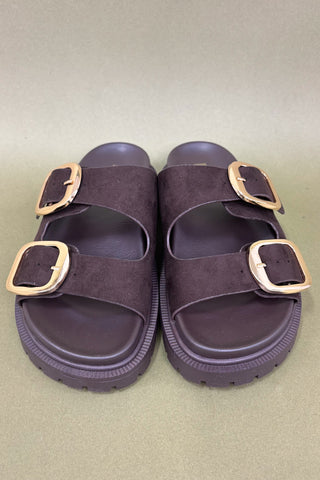 Pair of brown sandals with gold buckles on a beige background