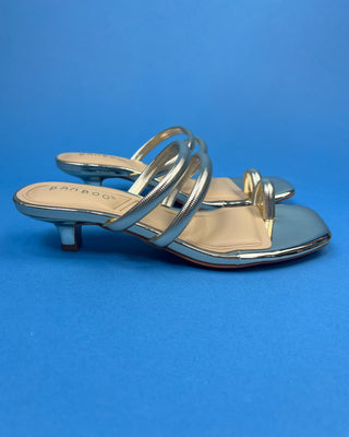 A pair of double strap slip on heels with square toes and low block heels, displayed on a solid blue background.