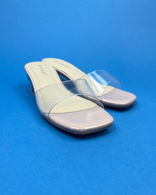A neutral pair of slip-on heels with a clear heel and clear strap on a blue background, 