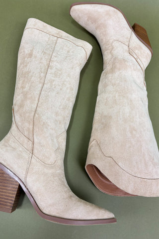 Pair of beige cowboy boots with brown soles on a green background