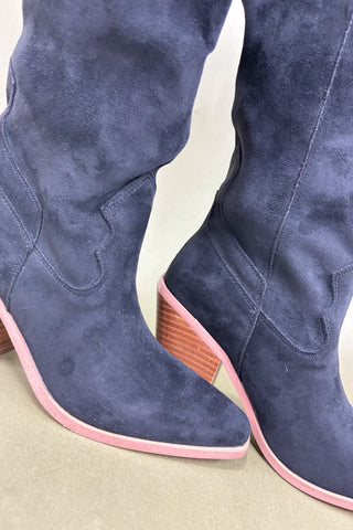 Navy blue suede boots with pink soles on a neutral background