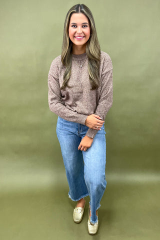 Woman wearing a brown sweater and blue jeans against a green background