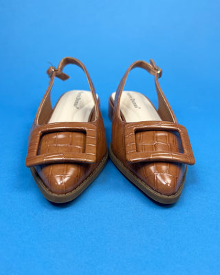 A pair of brown pointed-toe slingback flats with gold button accent against a solid blue background.