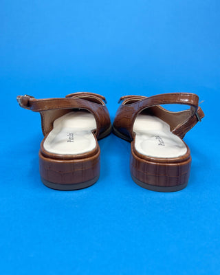 A pair of brown pointed-toe slingback flats with gold button accent against a solid blue background.