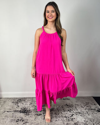 Model wearing a bright fuchsia tiered midi dress with braided halter neckline and flowy silhouette, styled with nude heeled sandals.