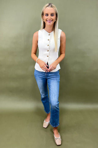 Woman wearing a white sleeveless top and blue jeans against a green background