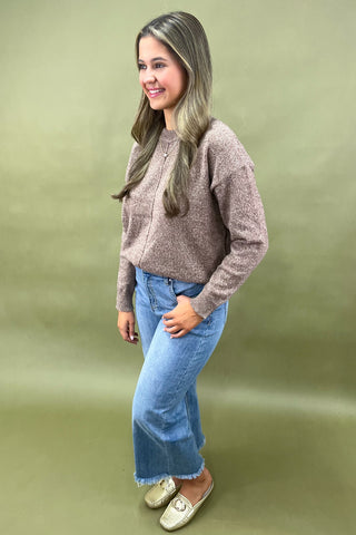 Woman wearing a brown cardigan and blue jeans against a green background