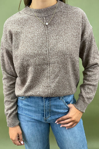 Person wearing a brown knitted sweater and blue jeans against a green background