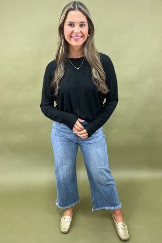 Woman wearing a black top and blue jeans against a green background