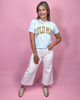 Person wearing a white t-shirt with gold text and white pants on a pink background
