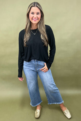 Woman wearing a black long-sleeve top and blue jeans against a green background