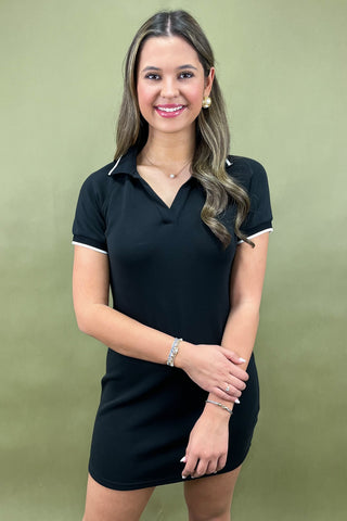 Woman wearing a black dress with white trim against a green background