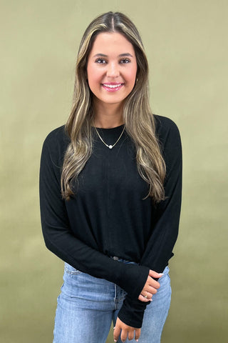 Woman wearing a black long-sleeve top and light blue jeans against a beige background