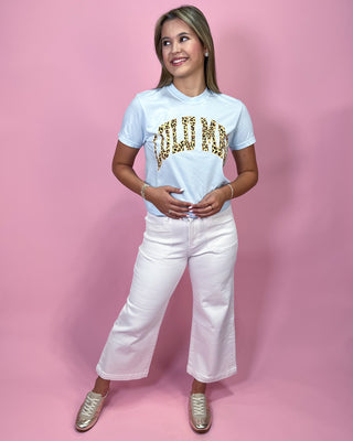 Woman wearing a white t-shirt with gold text and white pants on a pink background