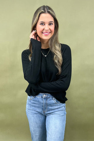 Woman wearing a black long-sleeve top and blue jeans against a green background