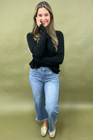 Woman wearing a black top and blue jeans against a green background