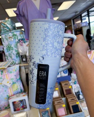 Person holding a blue patterned tumbler with 'ERA' branding in a store setting.