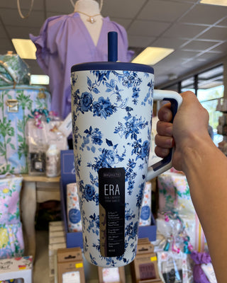 Floral-patterned mug with 'ERA' branding held by a person in a store setting.